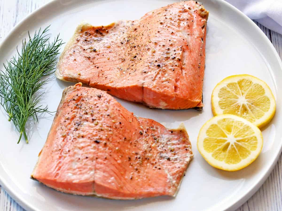 Two poached salmon fillets served on a white plate, garnished with dill and lemon slices. 