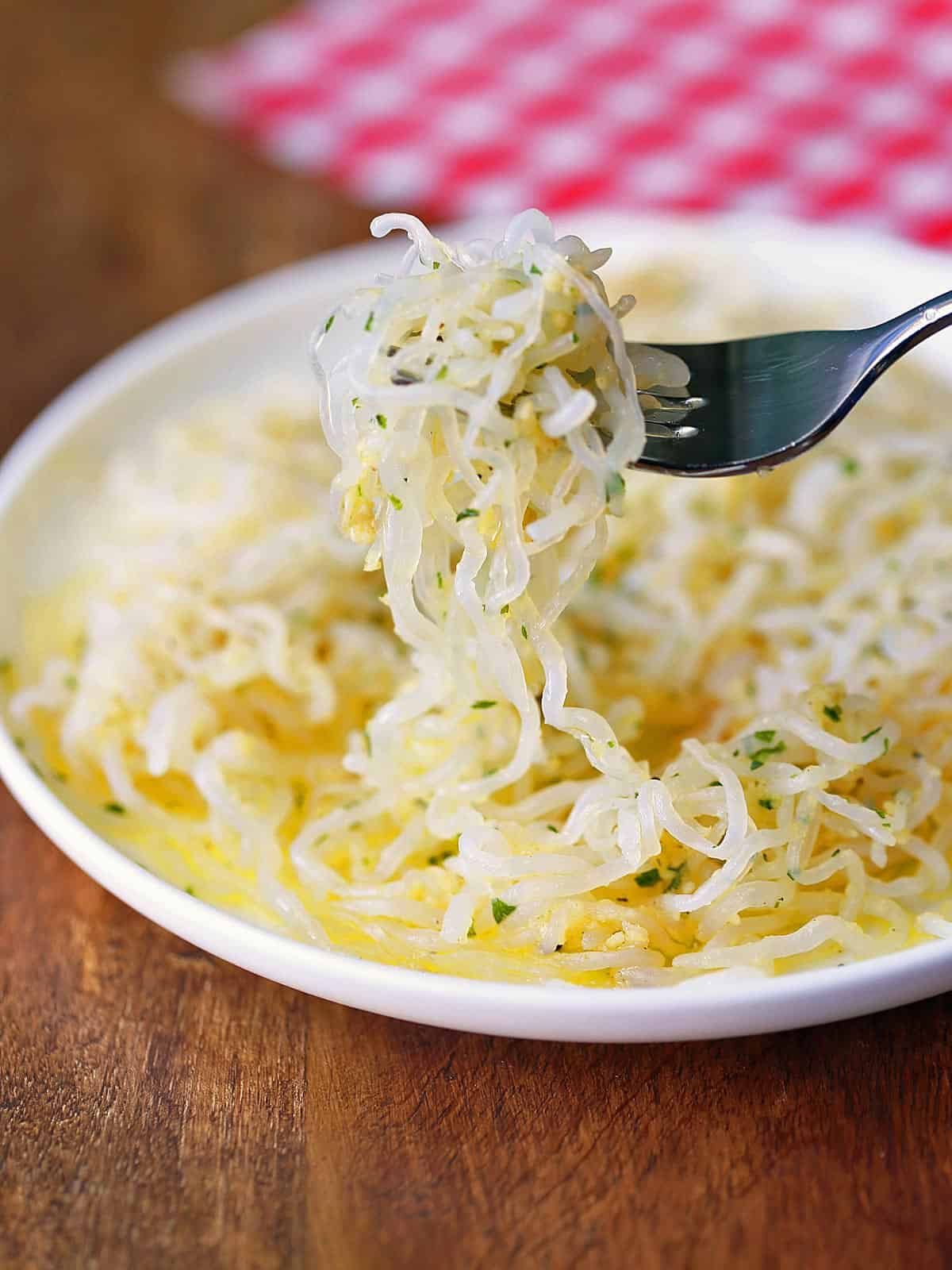 Shirataki noodles with butter and parmesan, served on a white plate with a fork. 