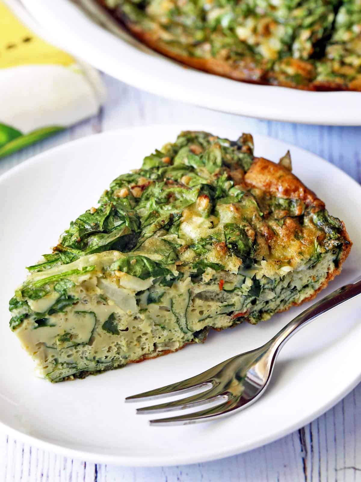 A slice of spinach frittata served on a plate with a fork.