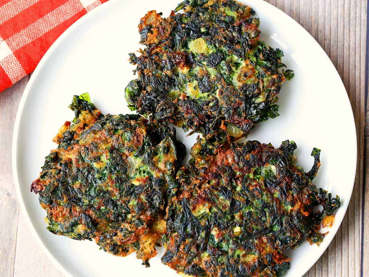 Three spinach fritters served on a white plate. 