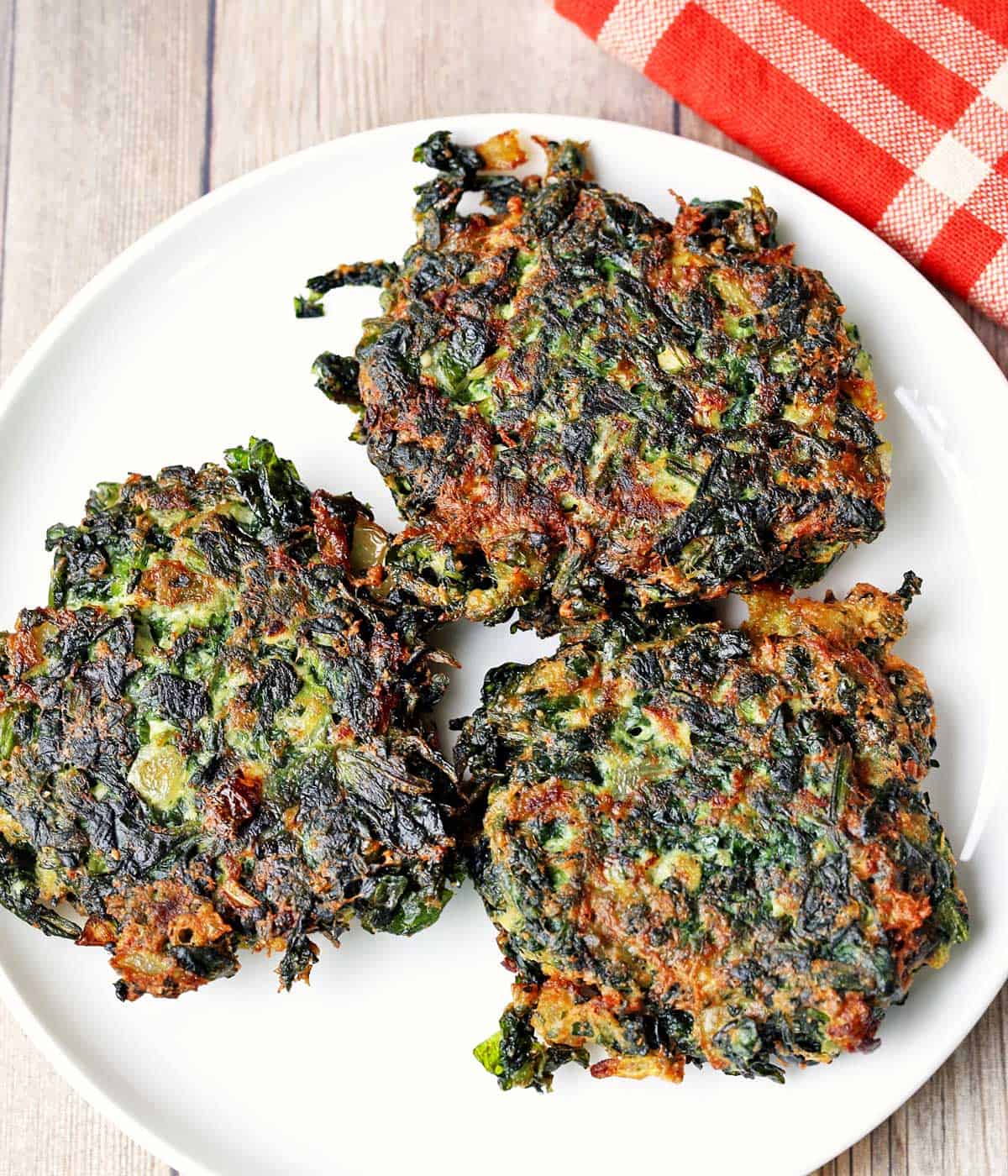 Three spinach fritters are served on a white plate with a red napkin. 