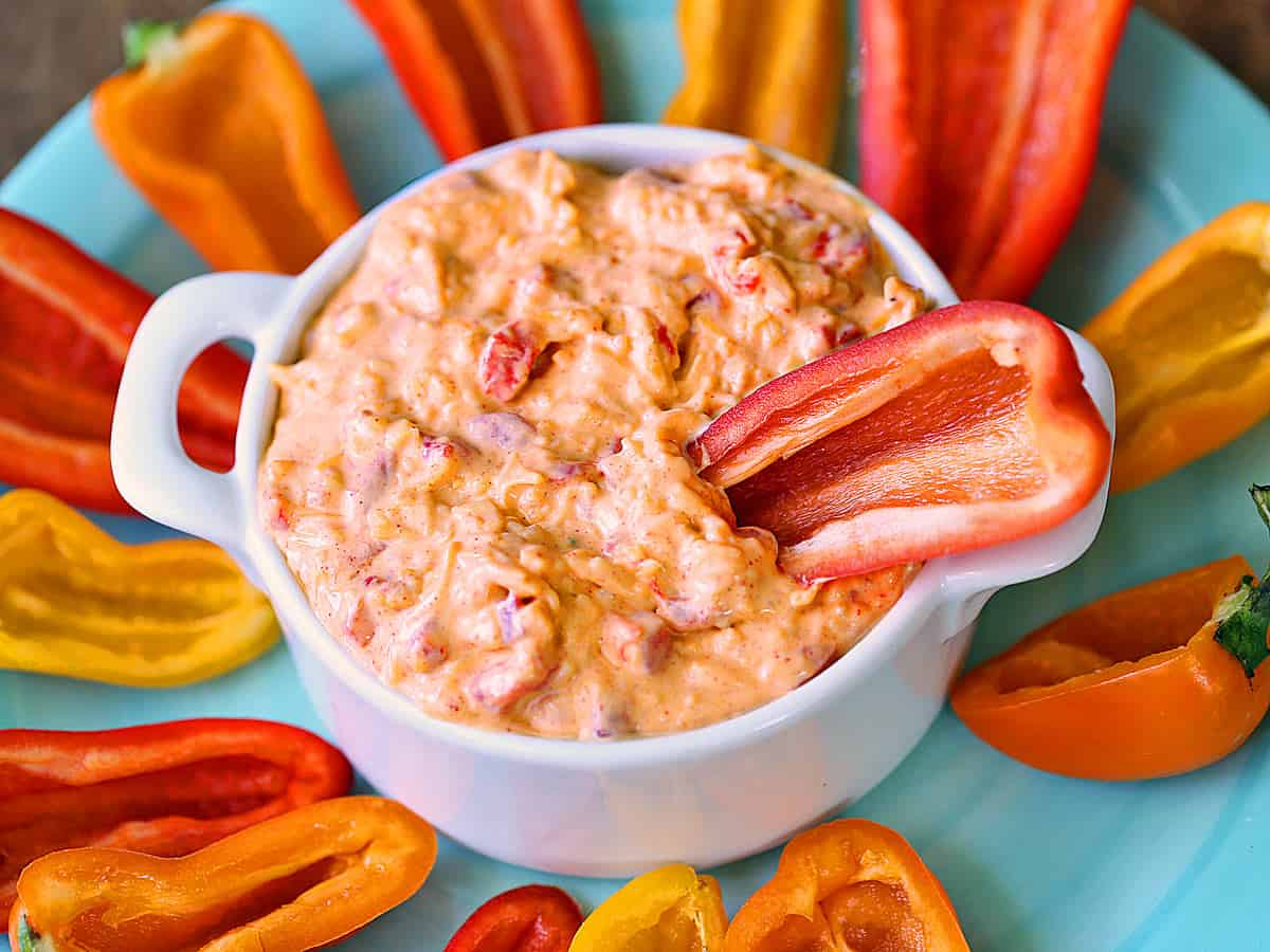 Pimento cheese in a white bowl, served with mini bell peppers. 