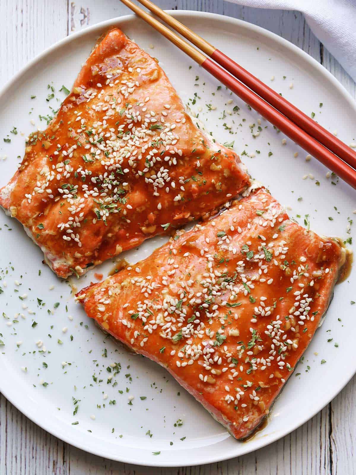 Two pieces of teriyaki salmon served on a white plate with chopsticks. 