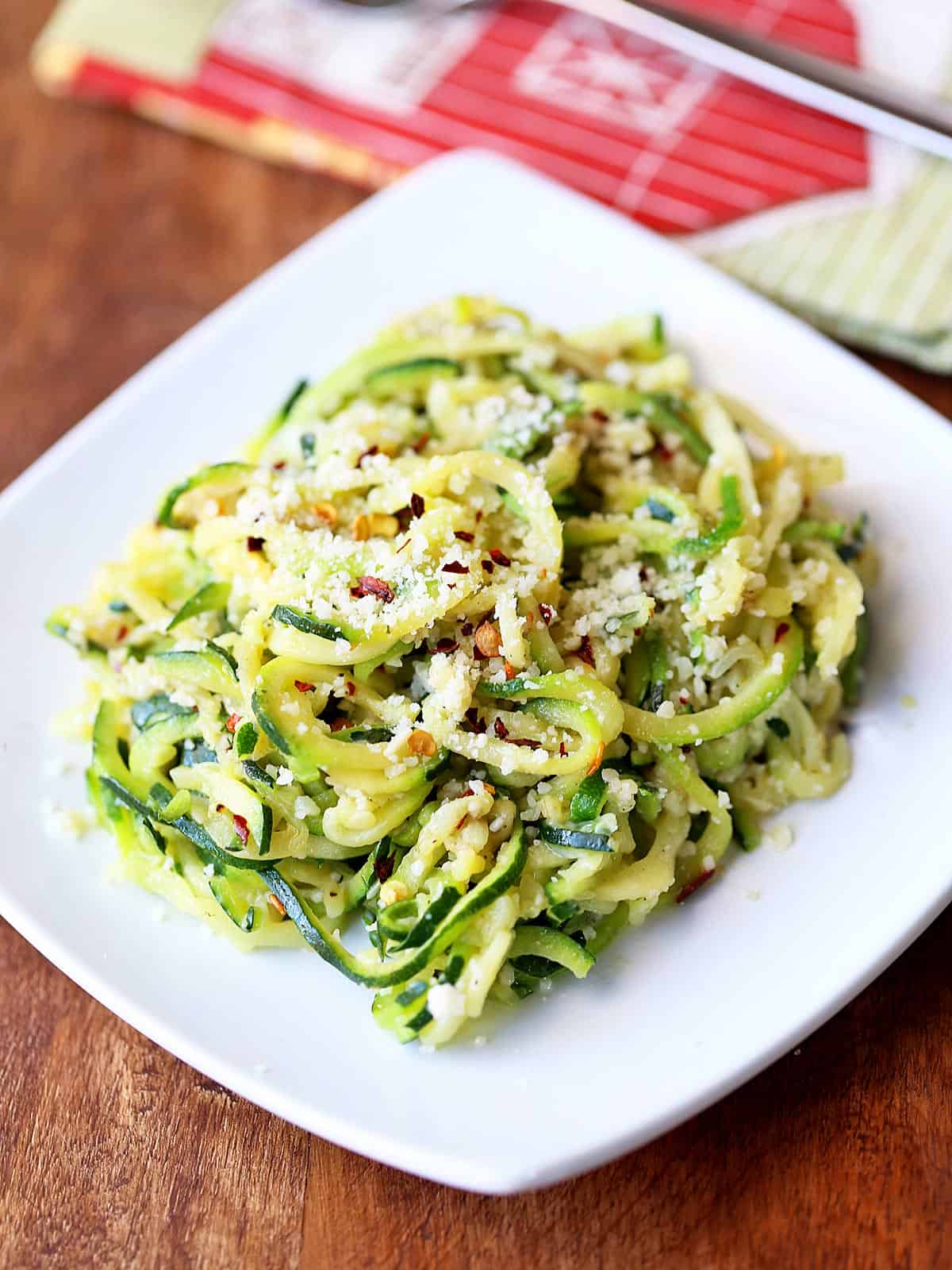 Buttered zucchini noodles served on a white plate with a napkin. 