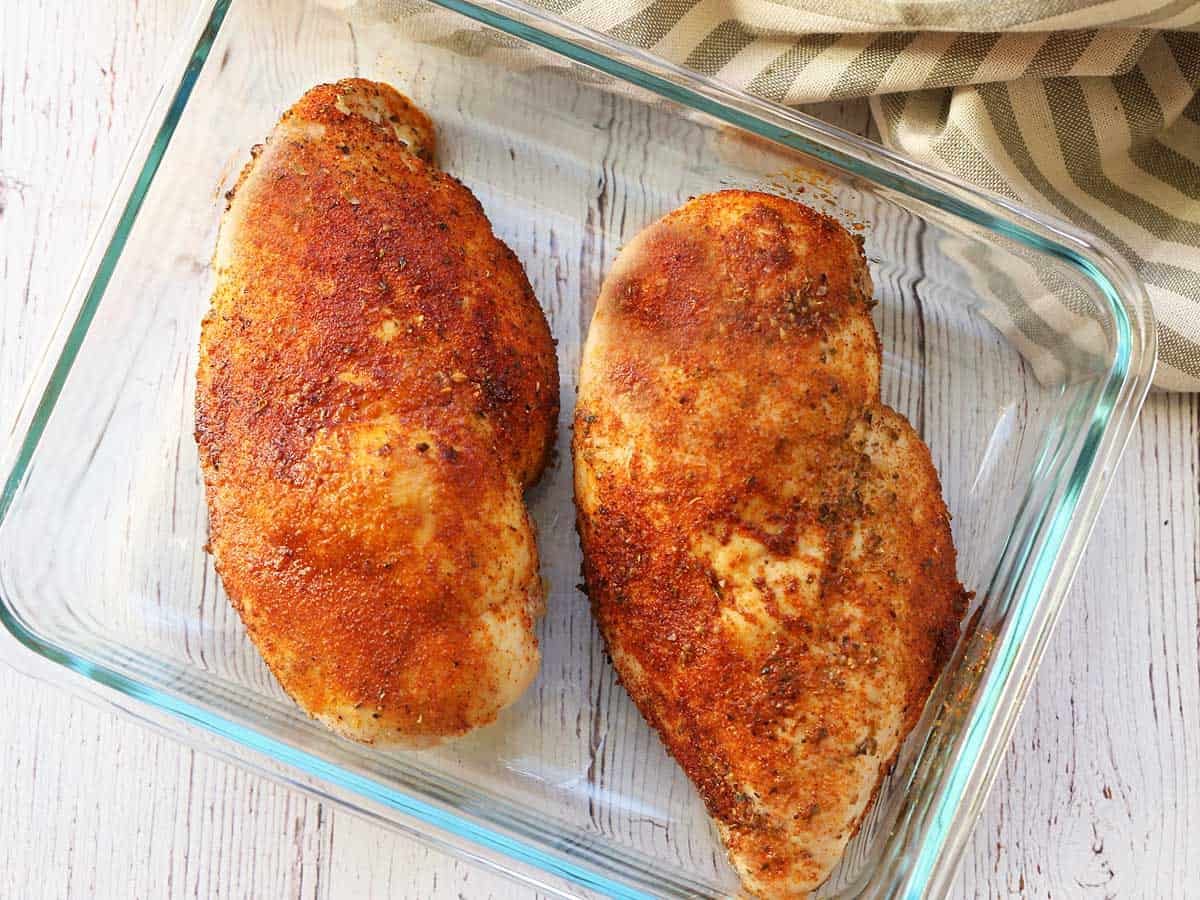 Leftover baked chicken breasts stored in a glass container. 