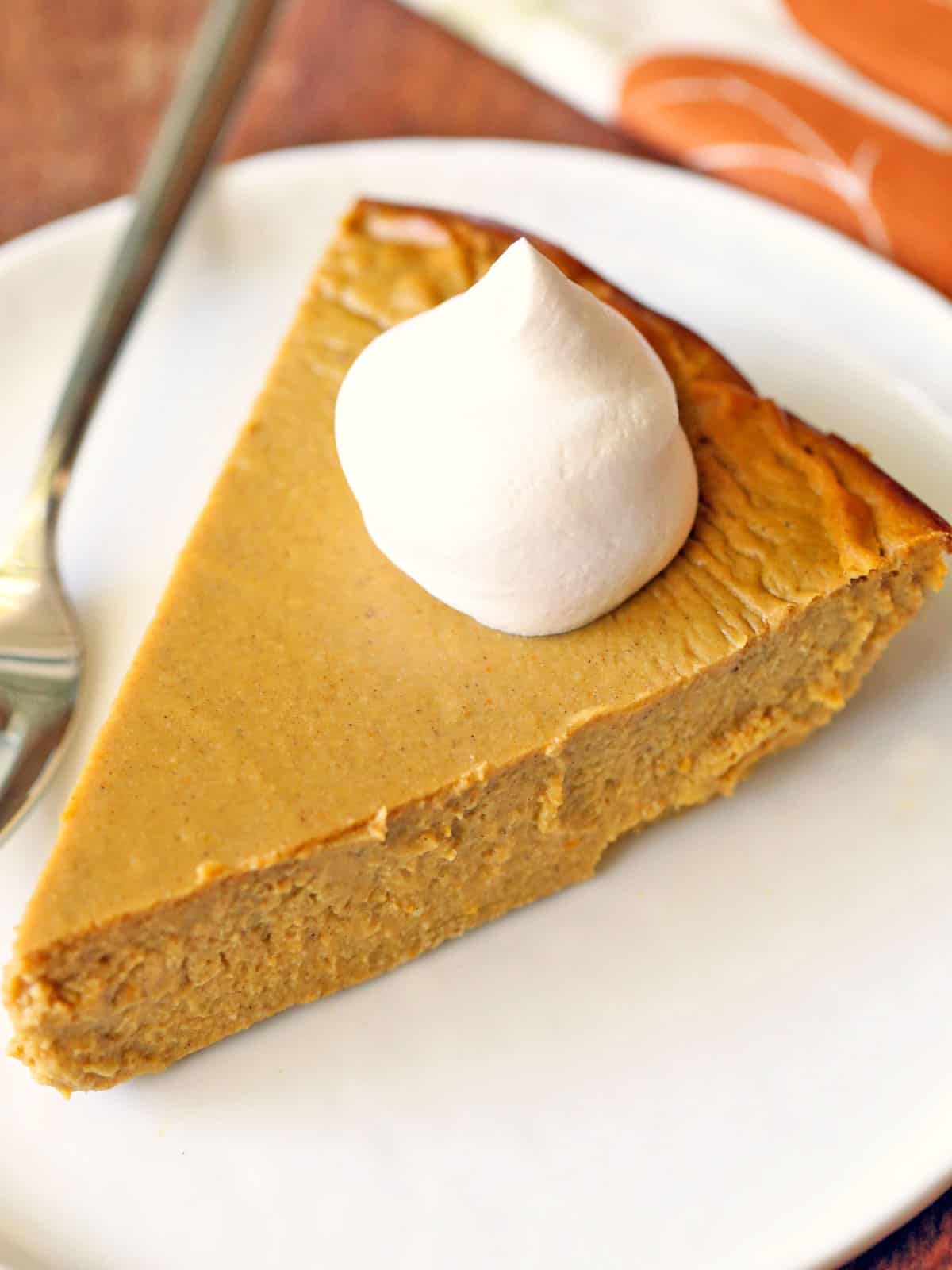 A slice of keto pumpkin pie is served on a white plate with a fork. 