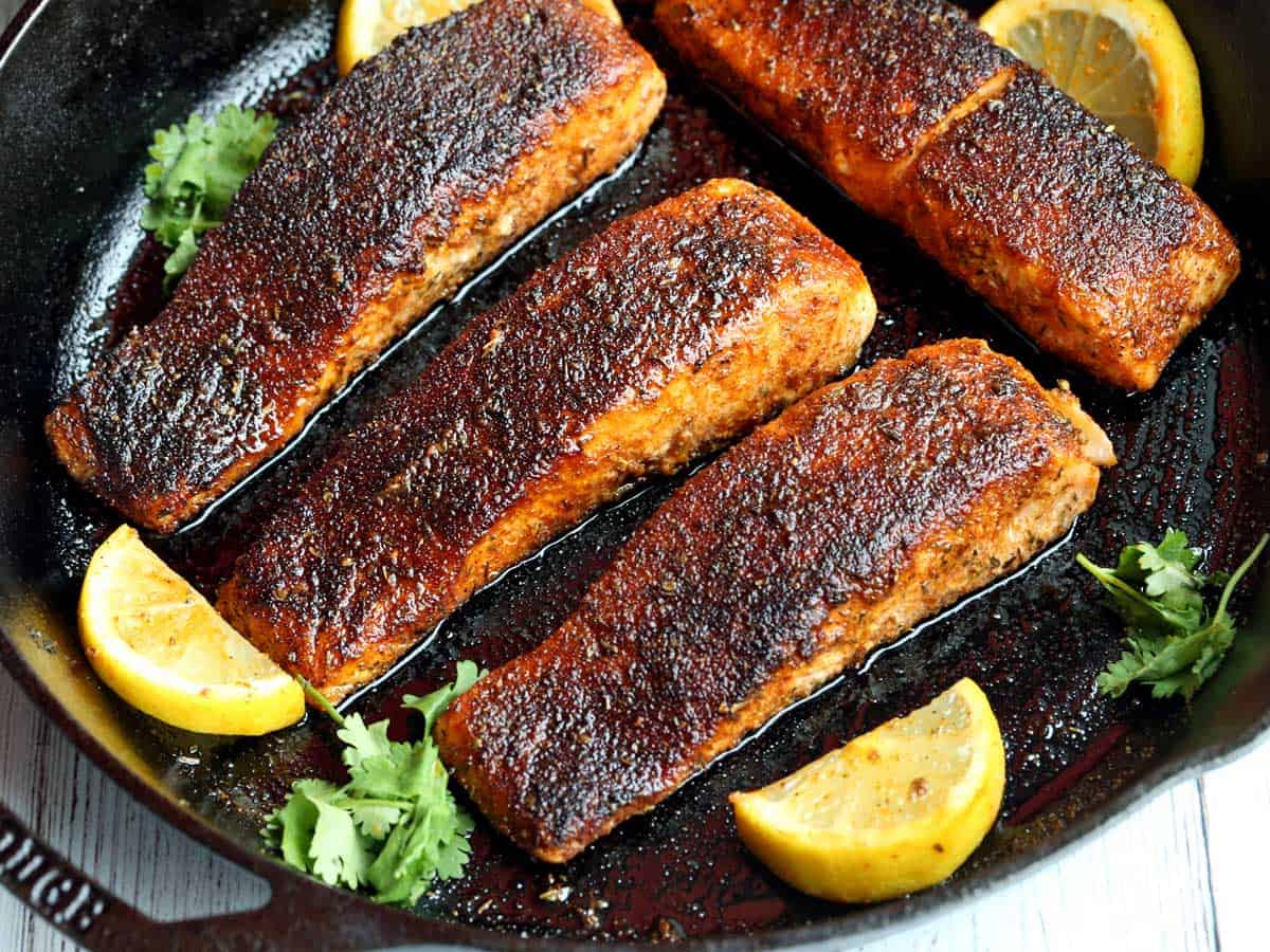 Four pieces of blackened salmon served in a cast-iron skillet. 