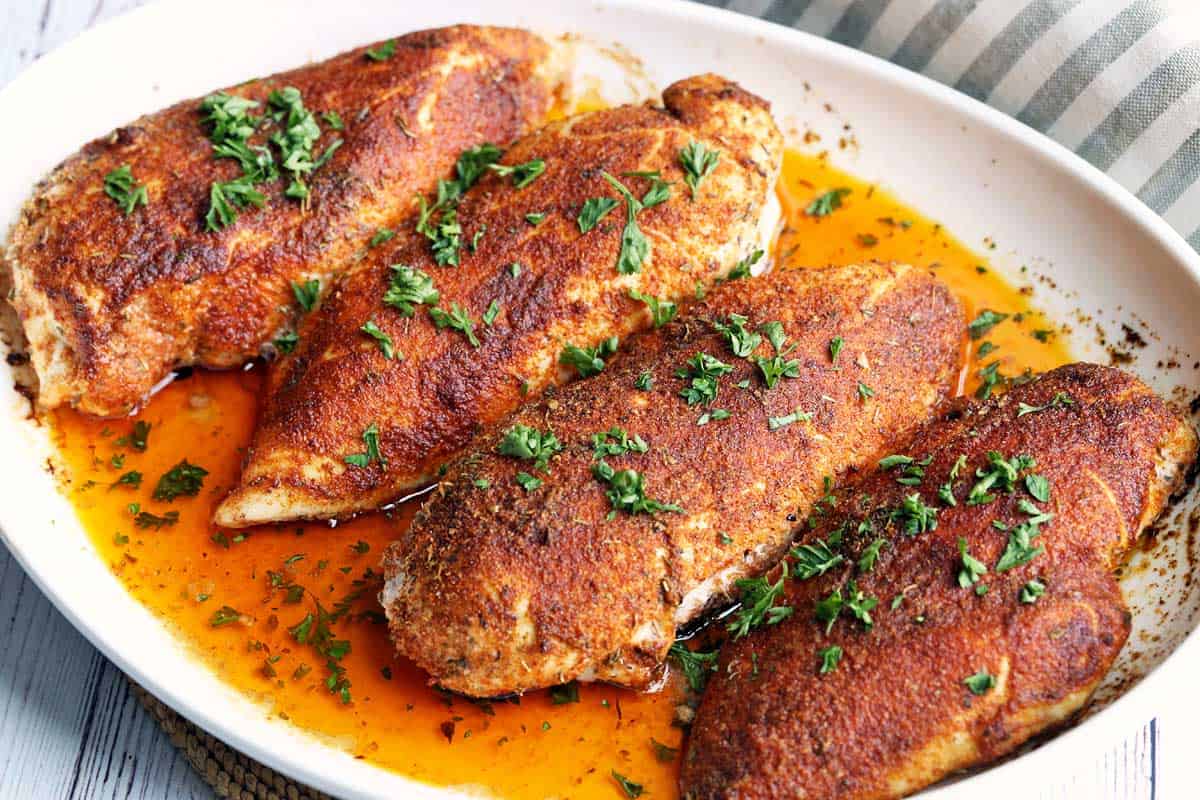 Four Cajun chicken breasts served in a white baking dish. 