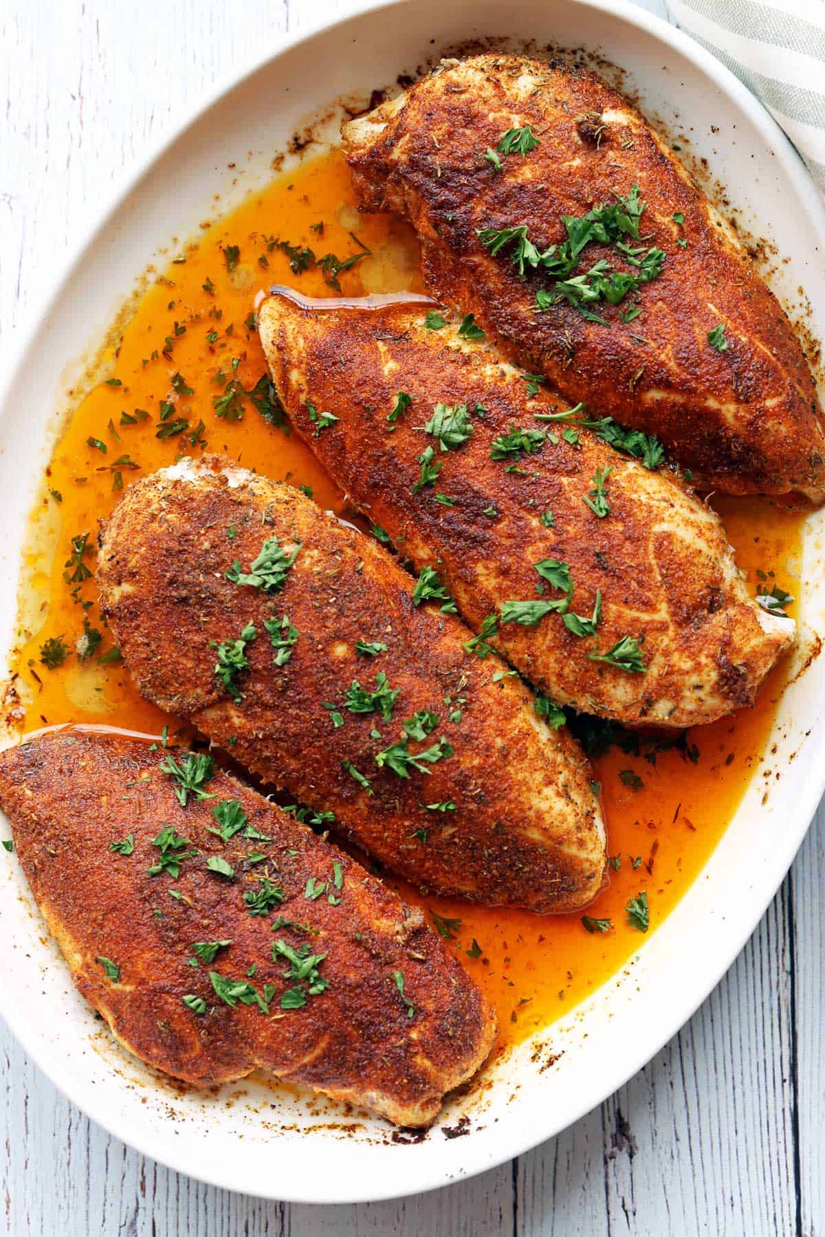 Four Cajun chicken breasts served in a white baking dish, topped with parsley. 