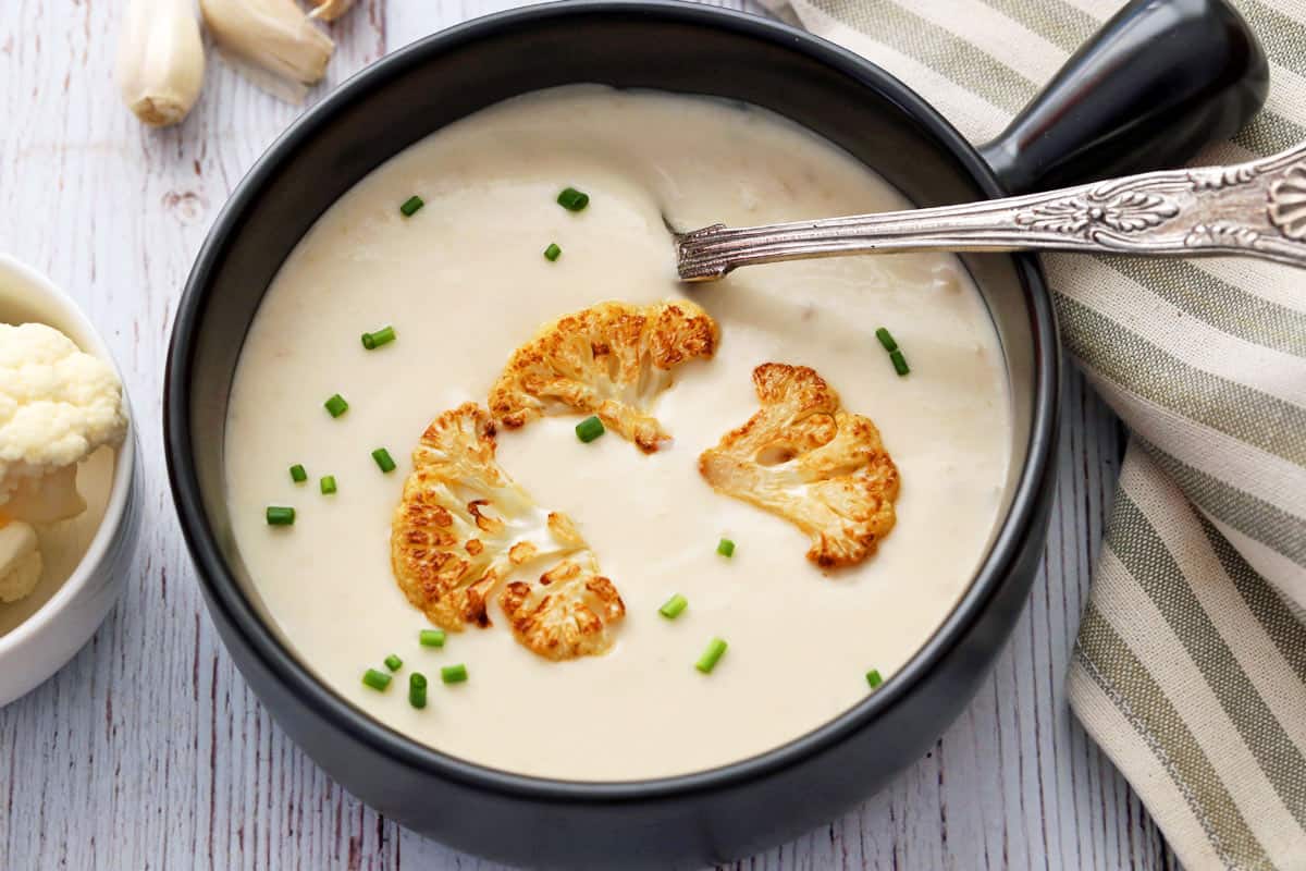 Creamy cauliflower soup served in a black soup bowl. 