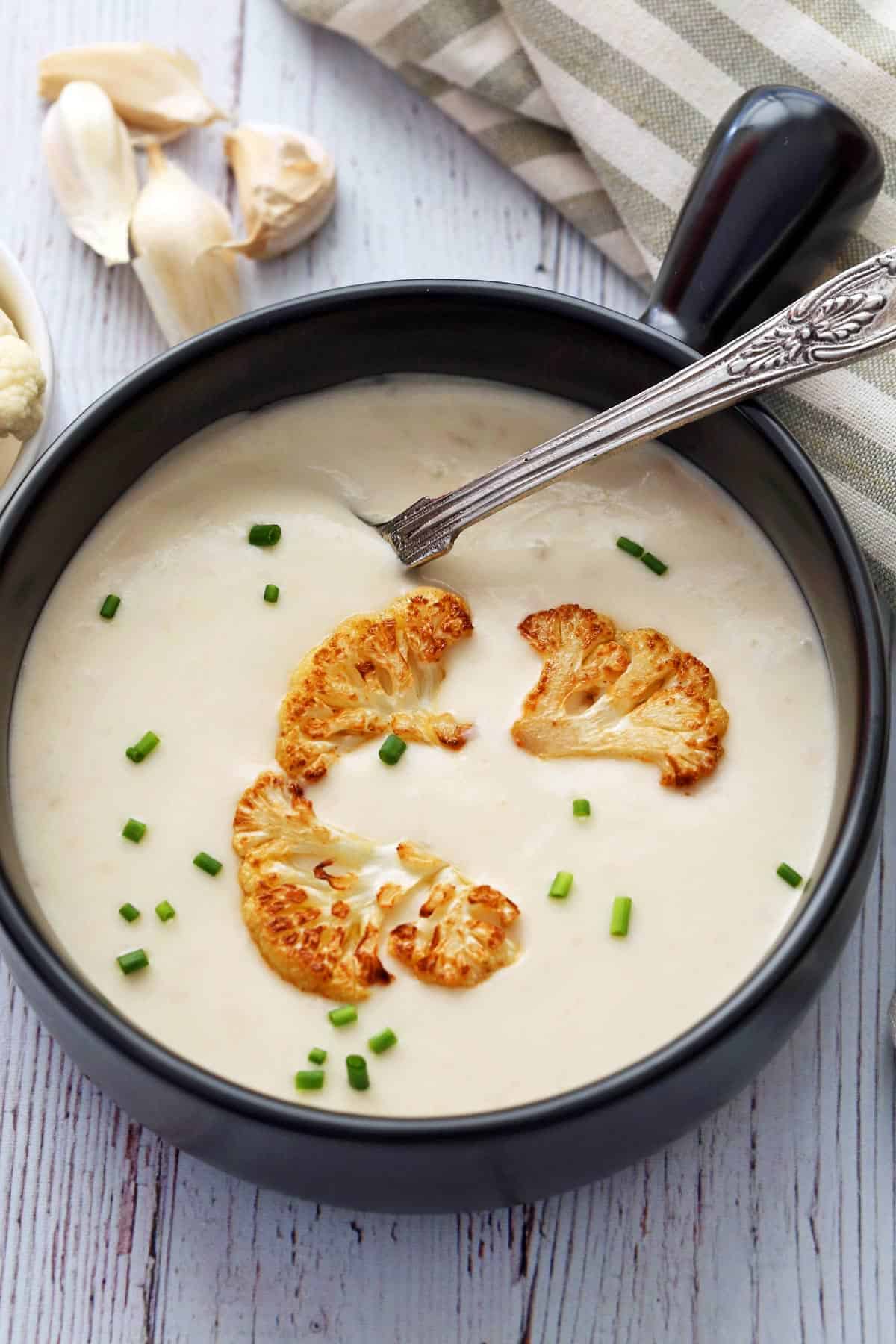 Cauliflower soup served in a black bowl. 
