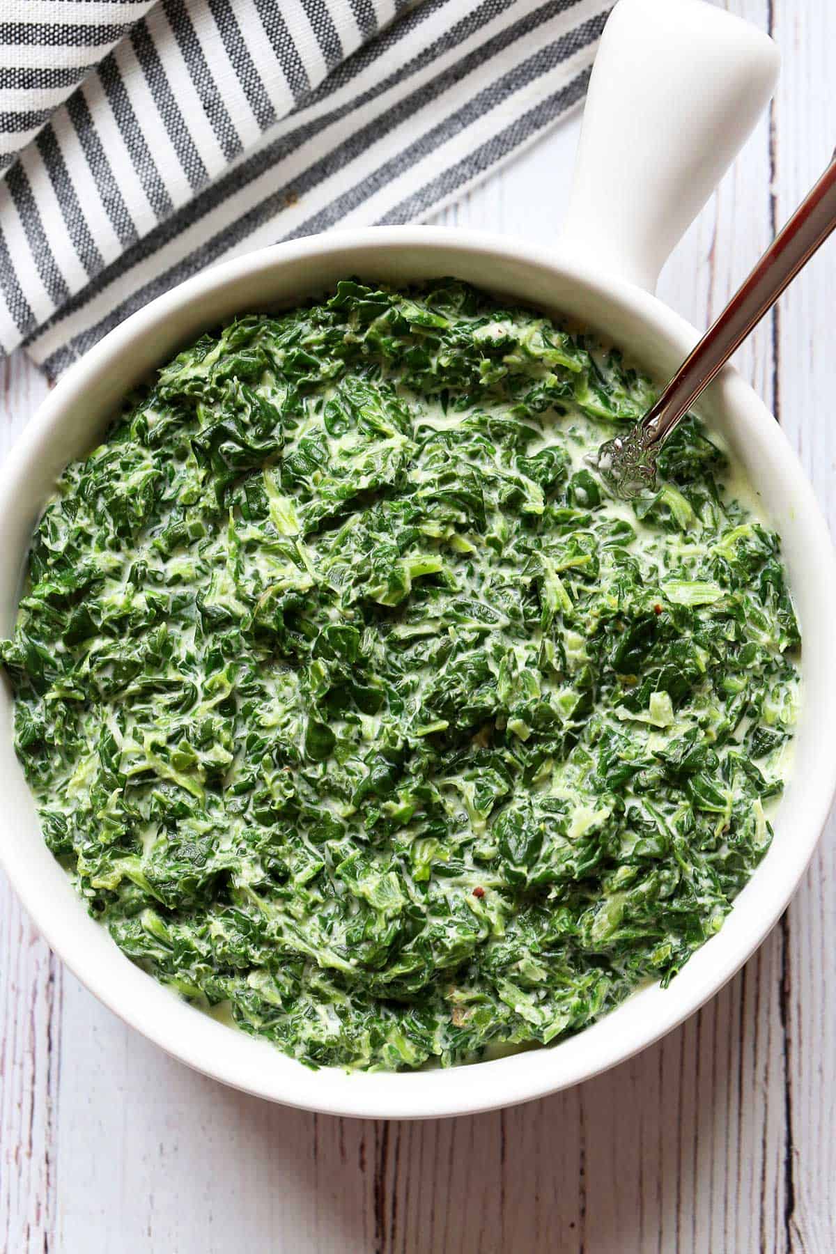 Creamed spinach served in a white bowl with a spoon. 