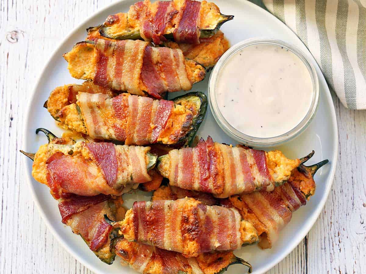 Jalapeno poppers served on a white plate with a dip. 