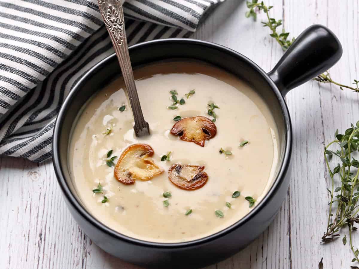 Cream of mushroom soup served in a black soup bowl with a spoon. 
