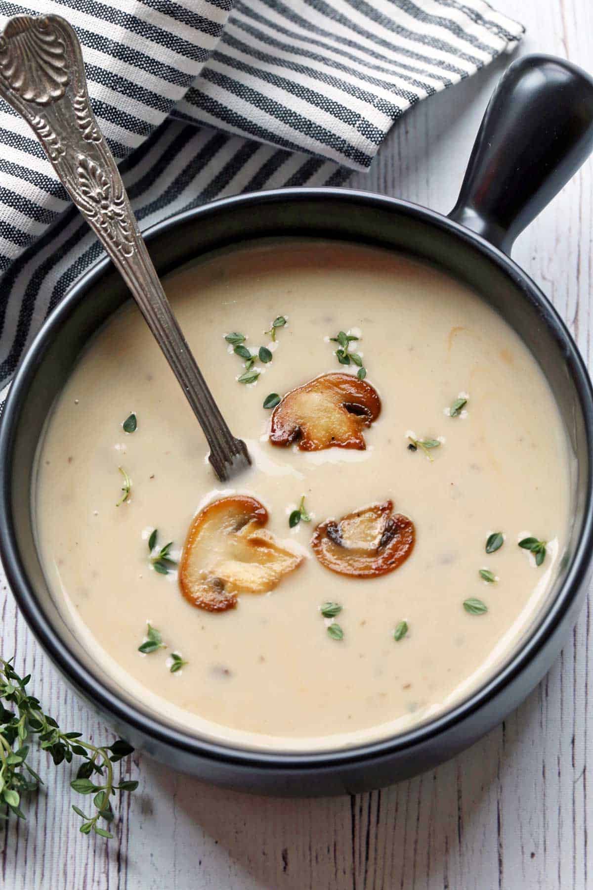 Cream of mushroom soup served in a black soup bowl and garnished with mushrooms.  