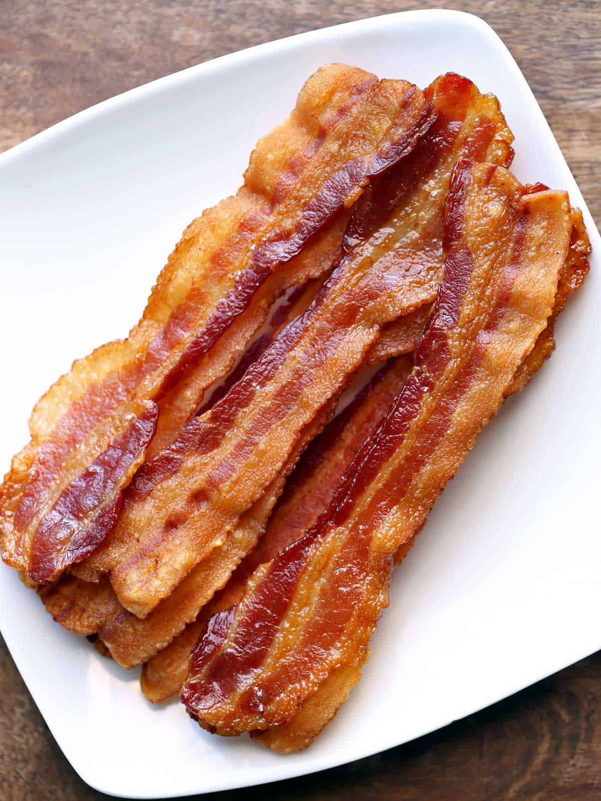 Slices of crispy oven bacon arranged on a white plate.  