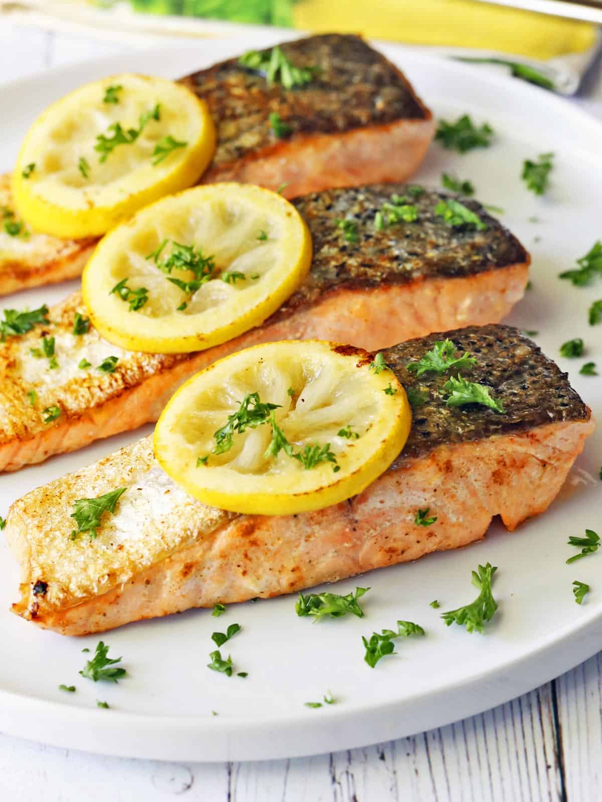 Three pan-fried salmon fillets topped with lemon slices and parsley.