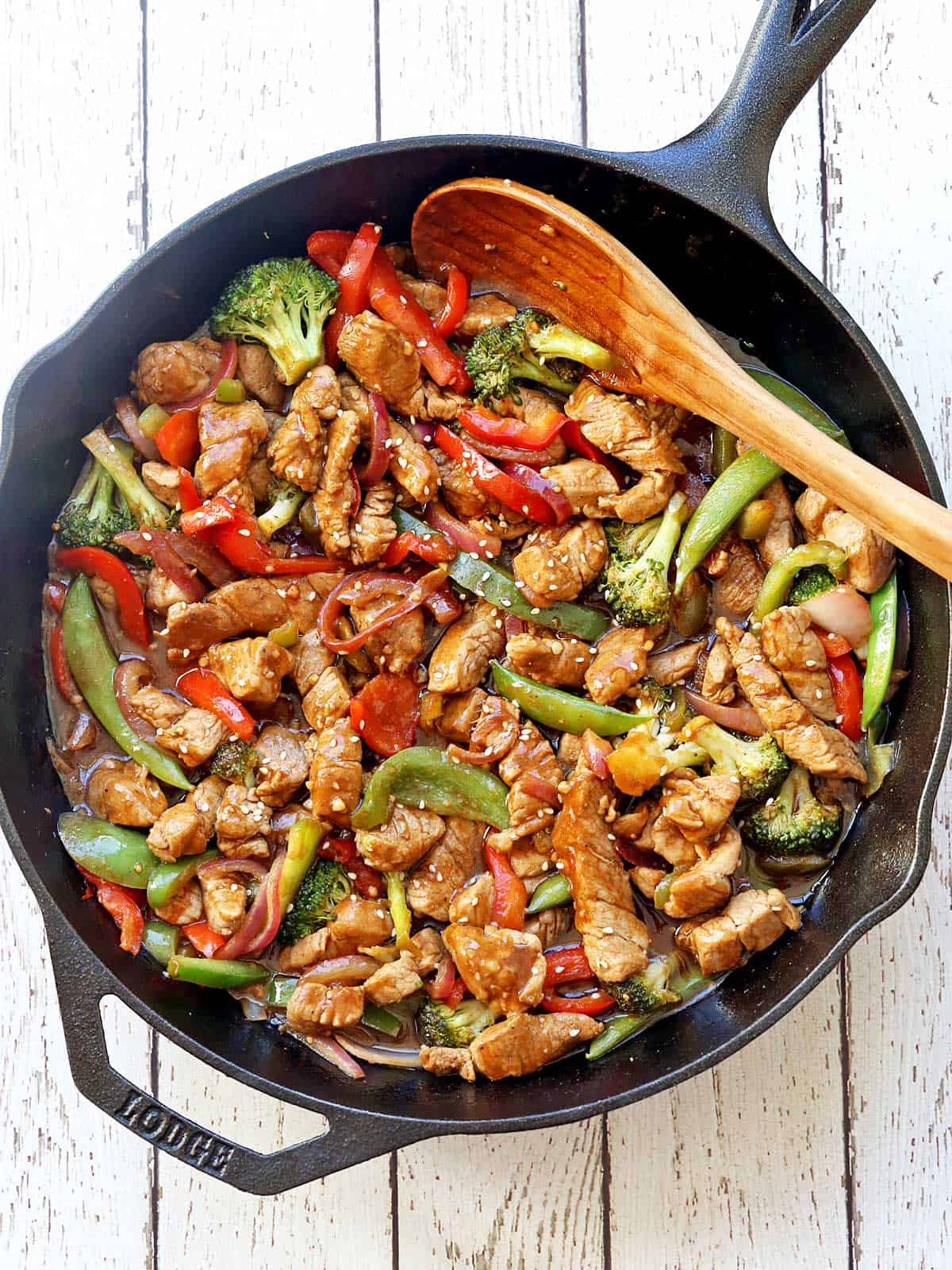 Pork stir-fry served in a skillet with a wooden spoon. 
