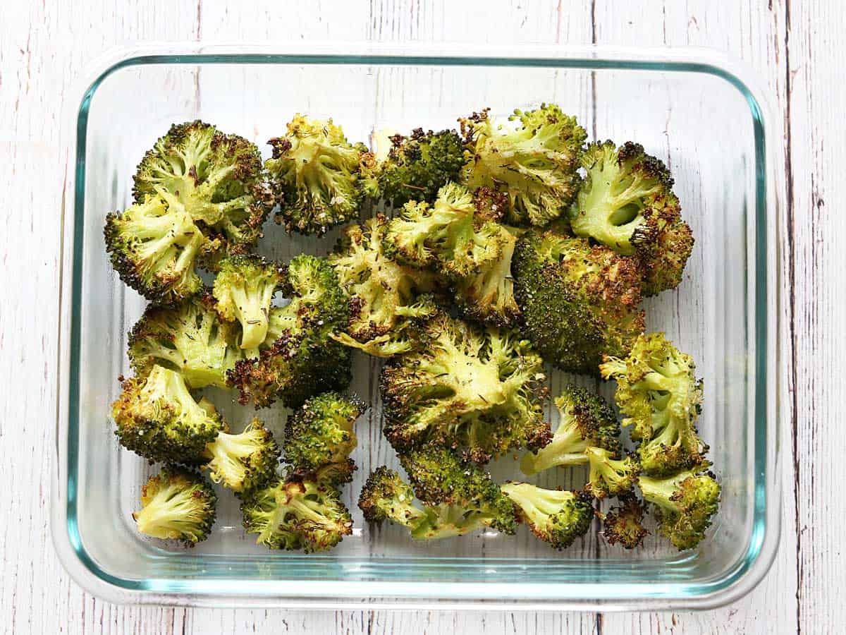Leftovers of oven-roasted broccoli stored in a glass container. 