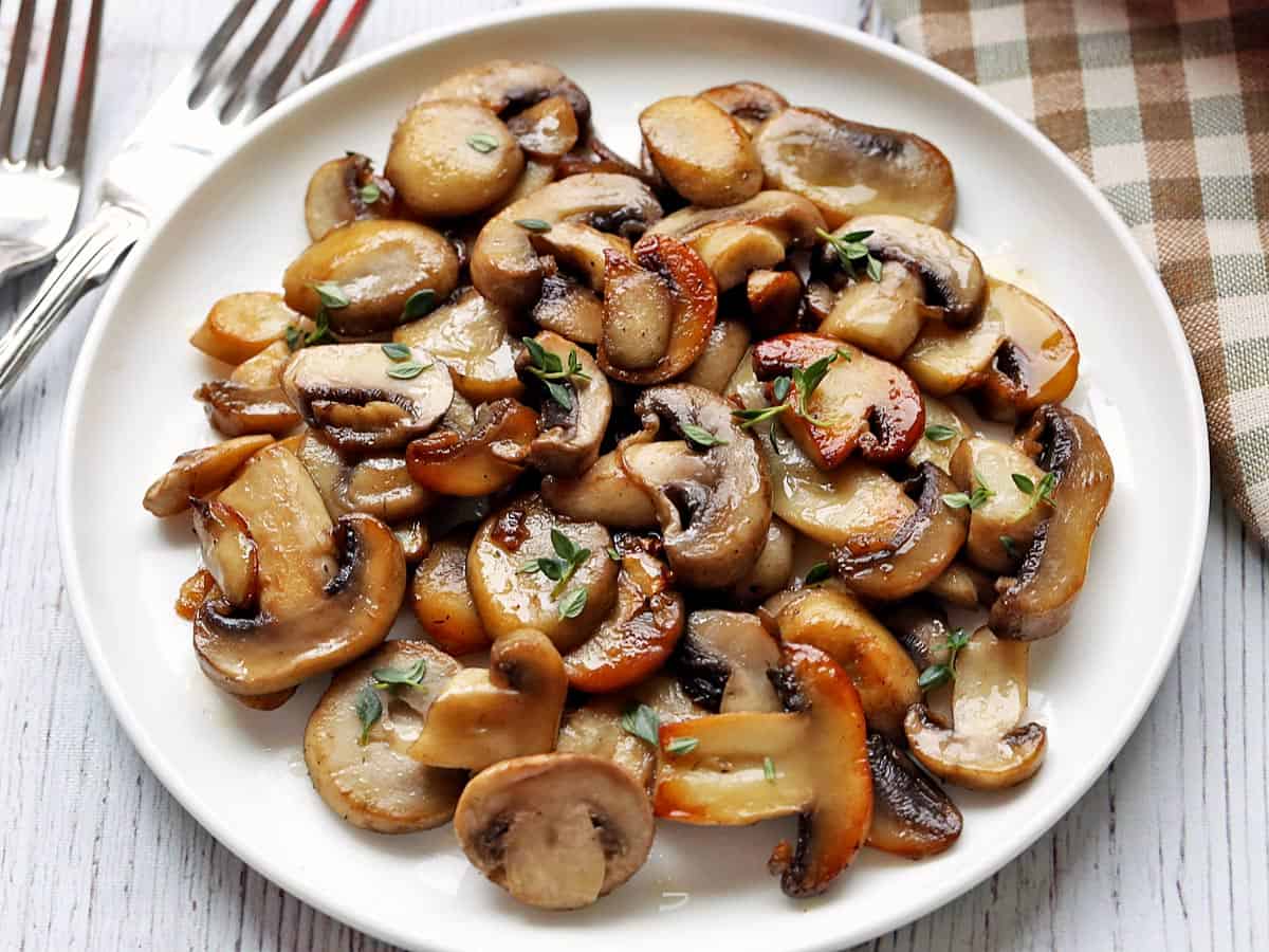 Sauteed mushrooms served on a white plate with a napkin and two forks. 
