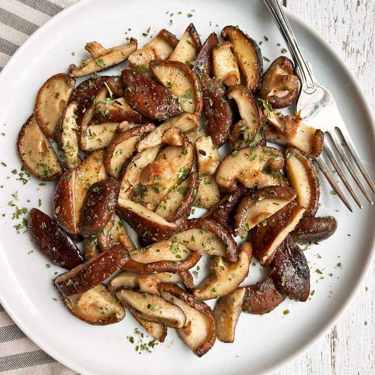 Sauteed shiitake mushrooms served on a white plate with a fork. 