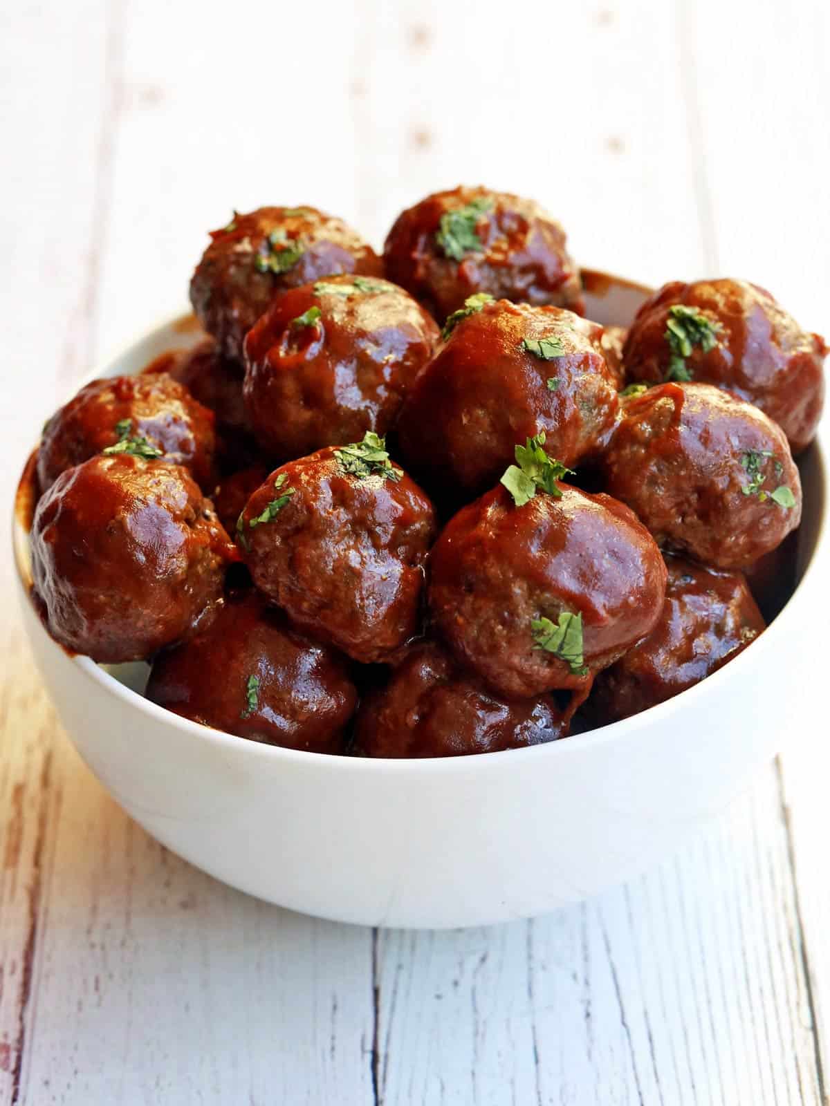 Sweet and sour meatballs served in a  white bowl with chopsticks. 