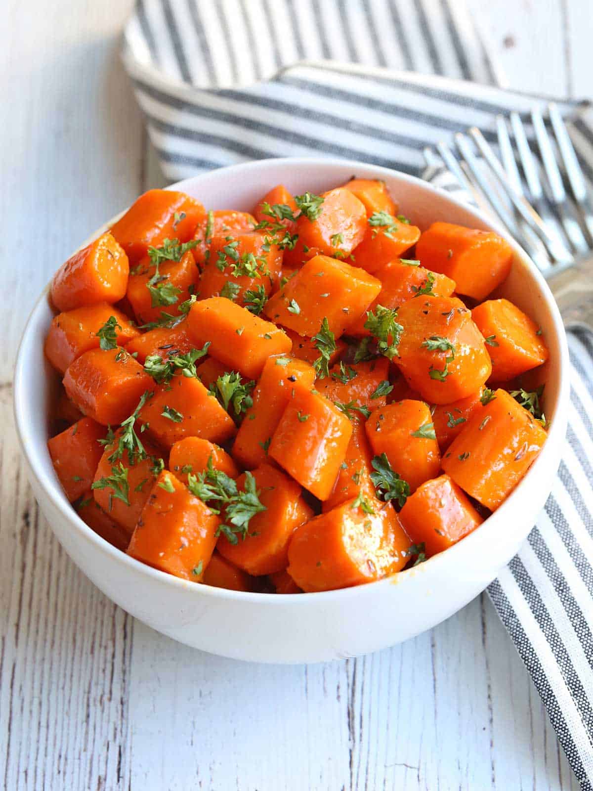 Glazed carrots served in a white bowl with forks. 