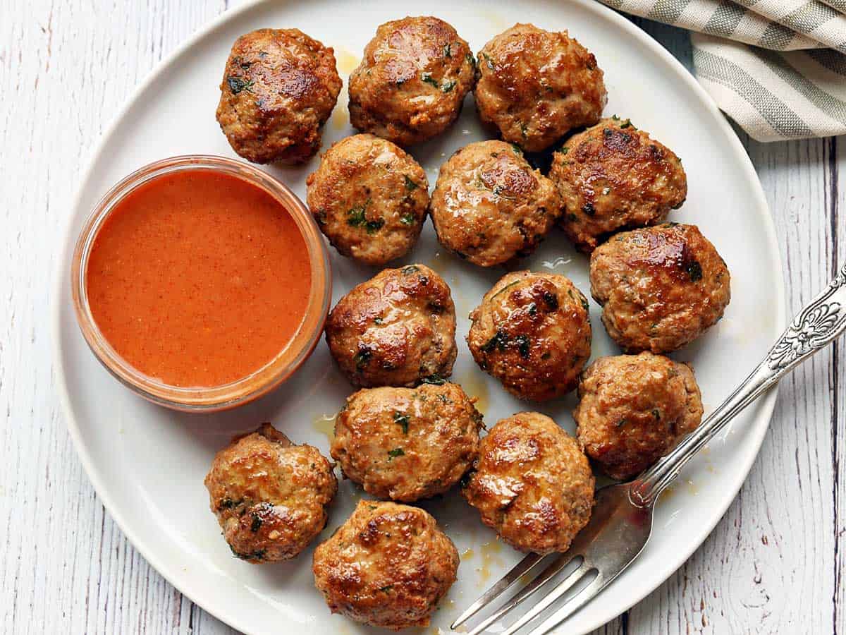 Turkey meatballs served on a white plate with a dipping sauce. 