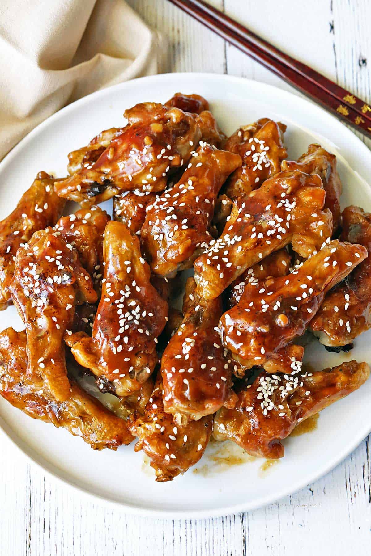 Teriyaki chicken wings topped with sesame seeds, served with chopsticks. 