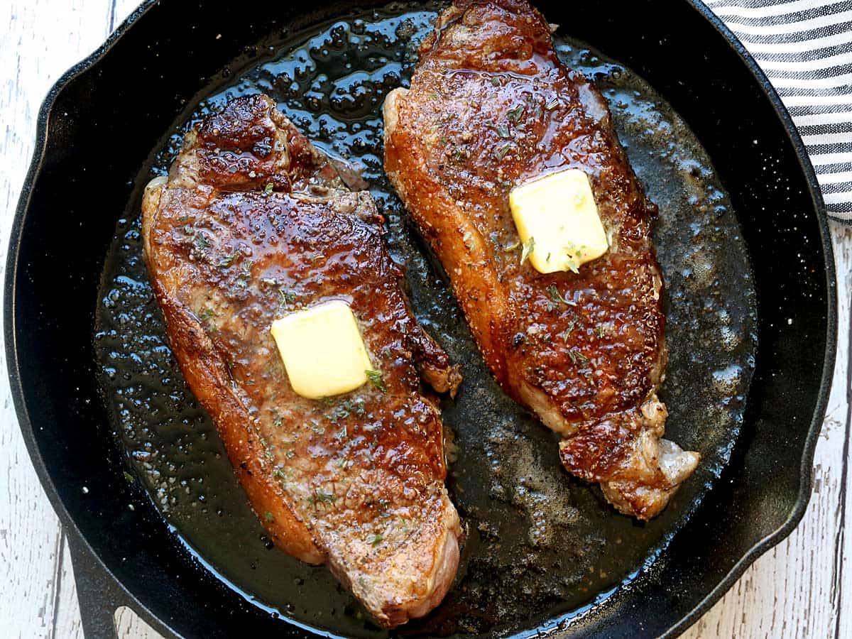 Two New York strip steaks served on a cast-iron skillet. 