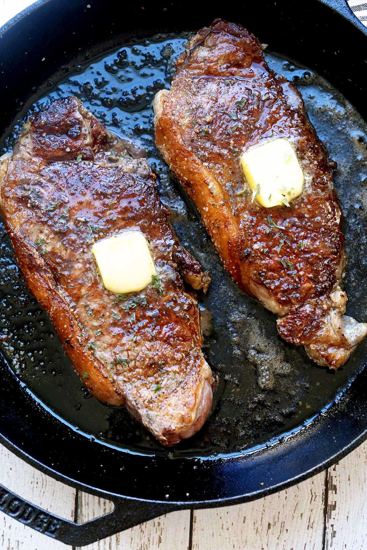 Two New York steaks served on a cast-iron skillet and topped with butter. 
