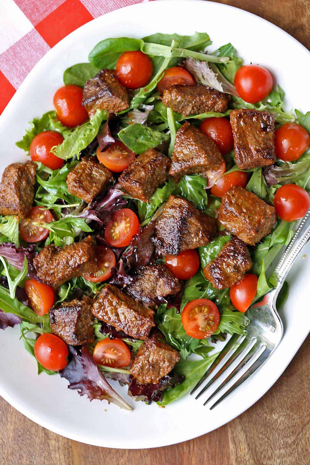 Steak salad with lettuce and tomatoes served on a white plate. 