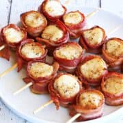 Bacon-wrapped scallops served on a white plate.