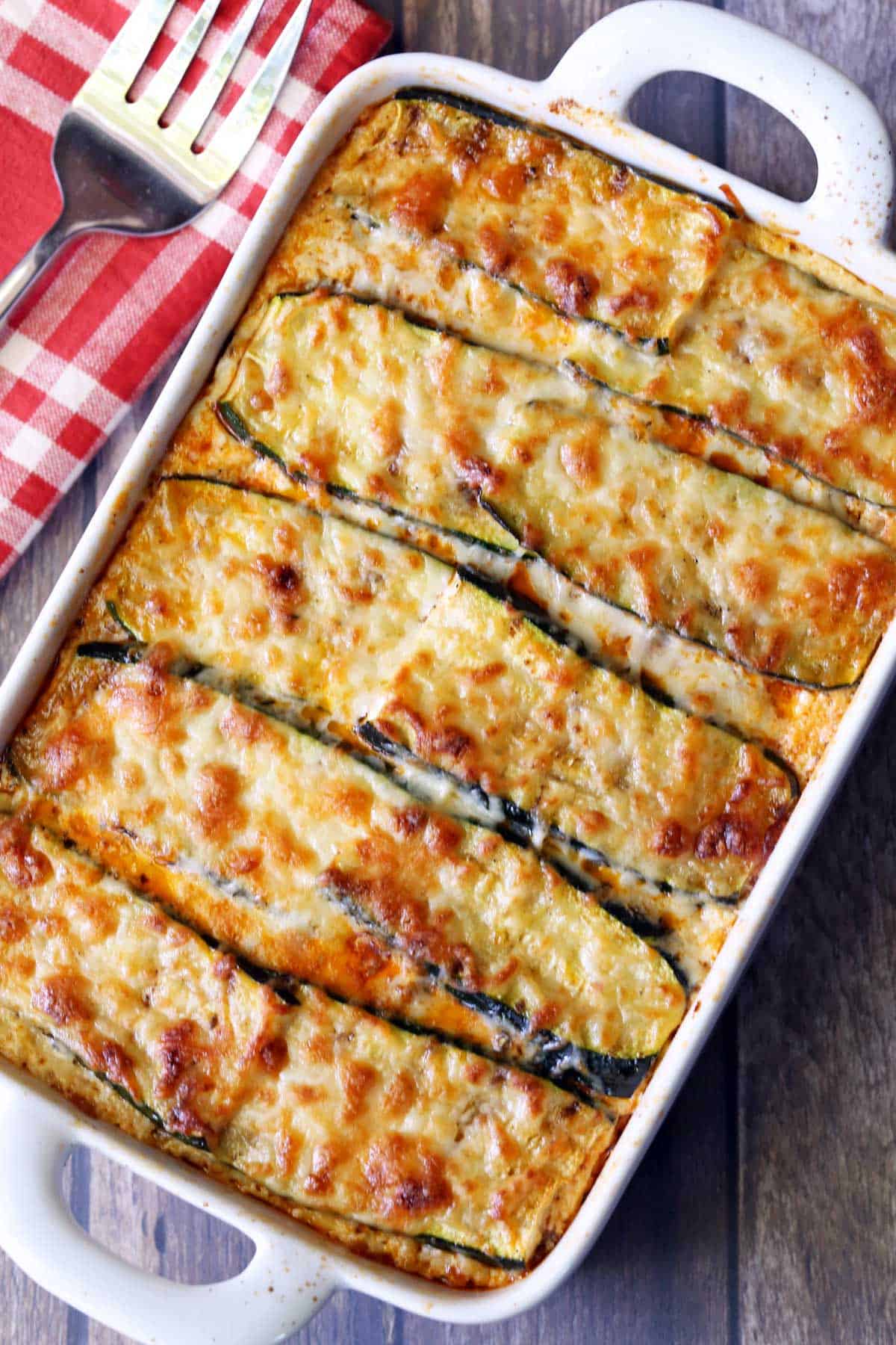 Zucchini lasagna is served in a white baking dish with a serving fork. 