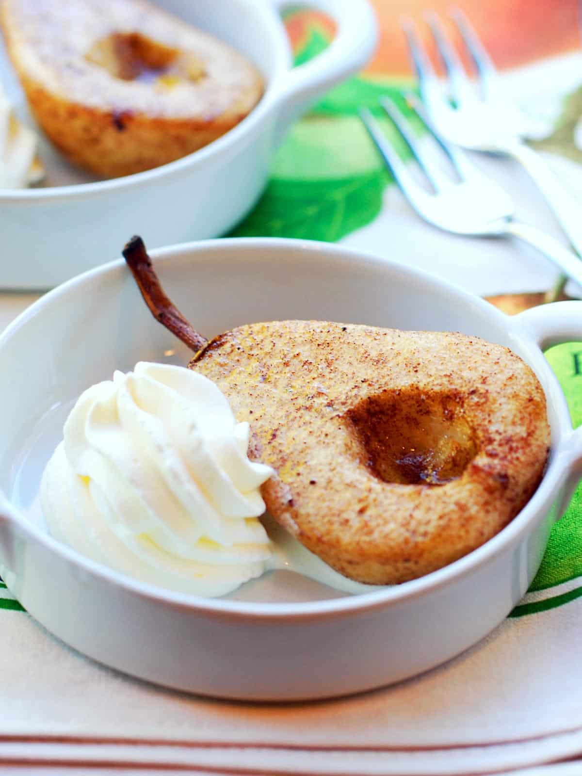 Baked pears served in a white baking dish with whipped cream. 