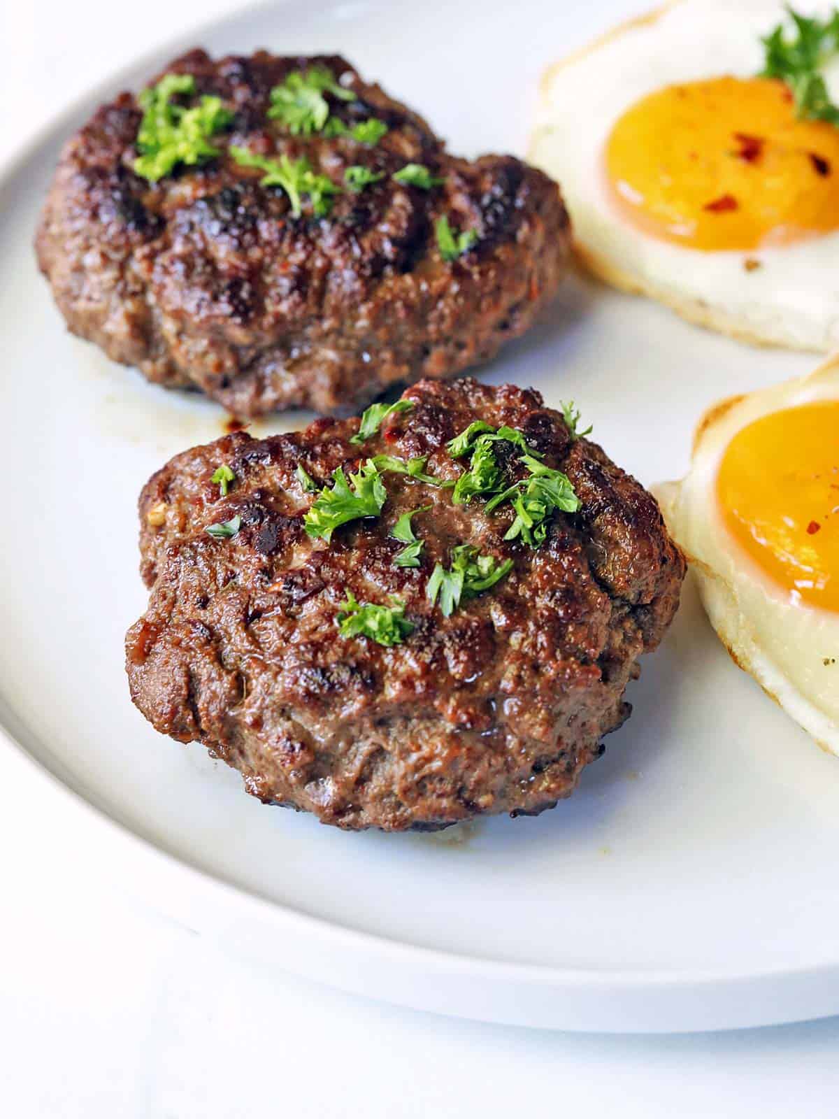 Two beef sausage patties served with fried eggs. 