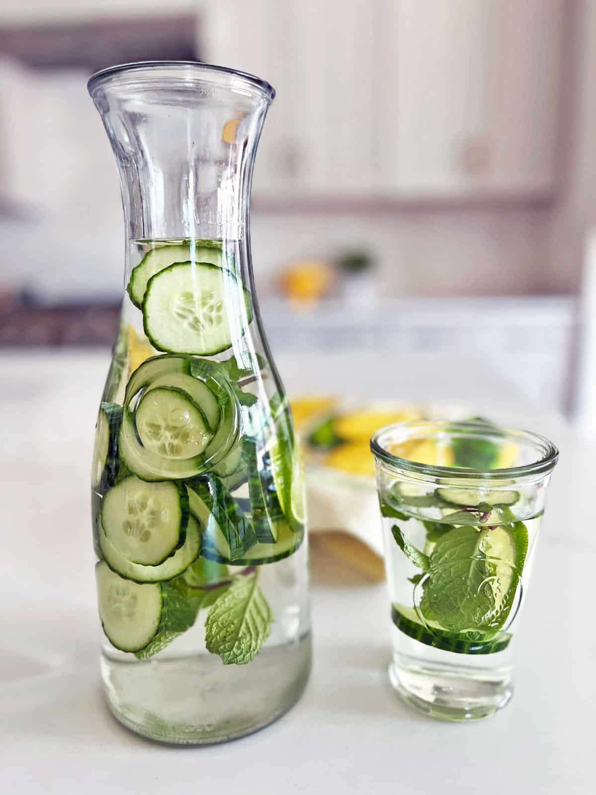 A pitcher and a glass filled with cucumber water. 