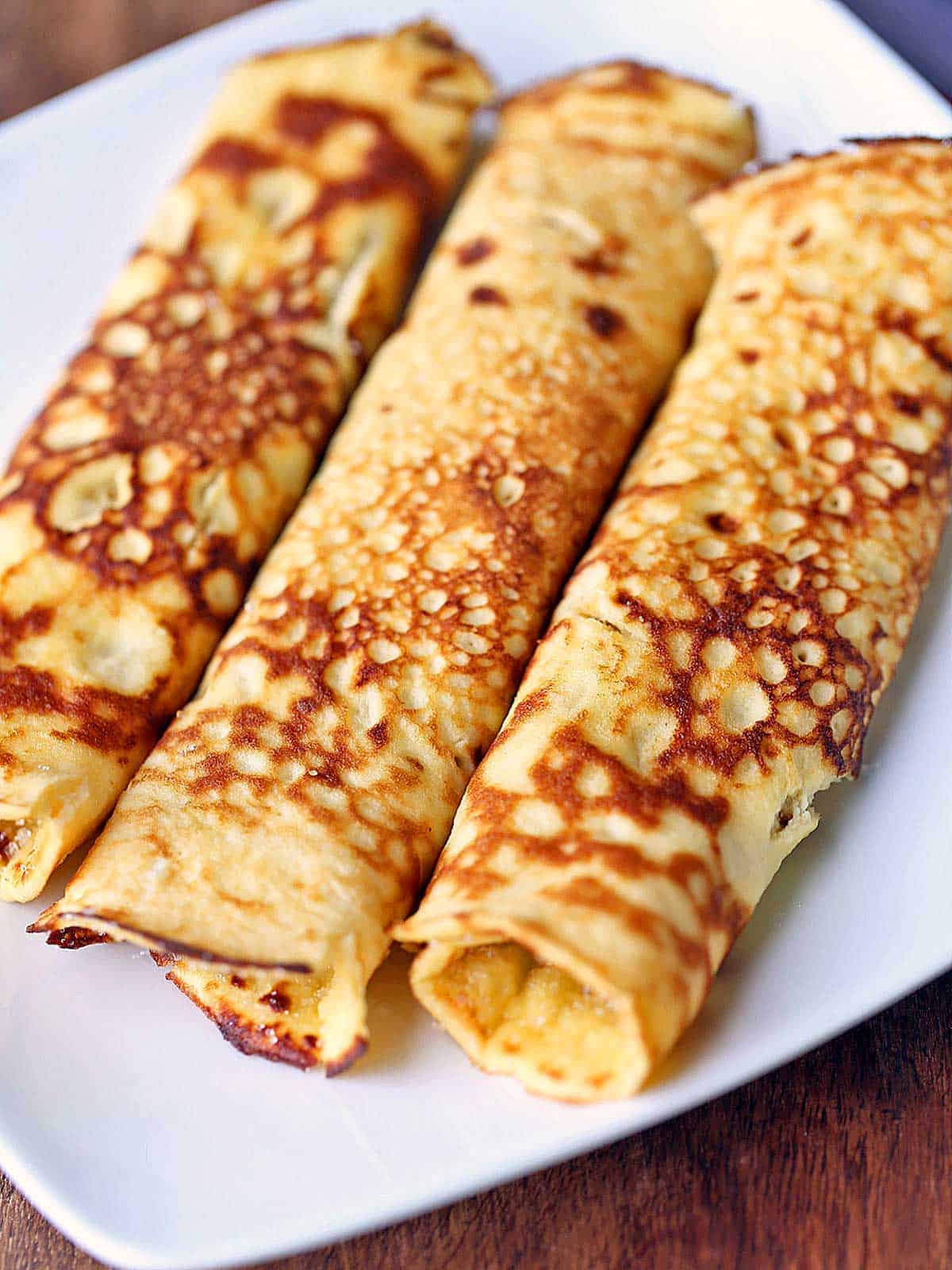 Three pannenkoeken rolled up and served on a white plate. 