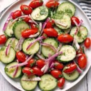 Cucumber tomato salad served on a white plate with a striped napkin.