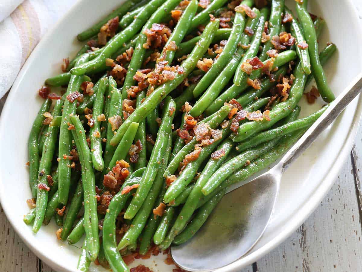 Green beans with bacon served on a platter with a serving spoon. 