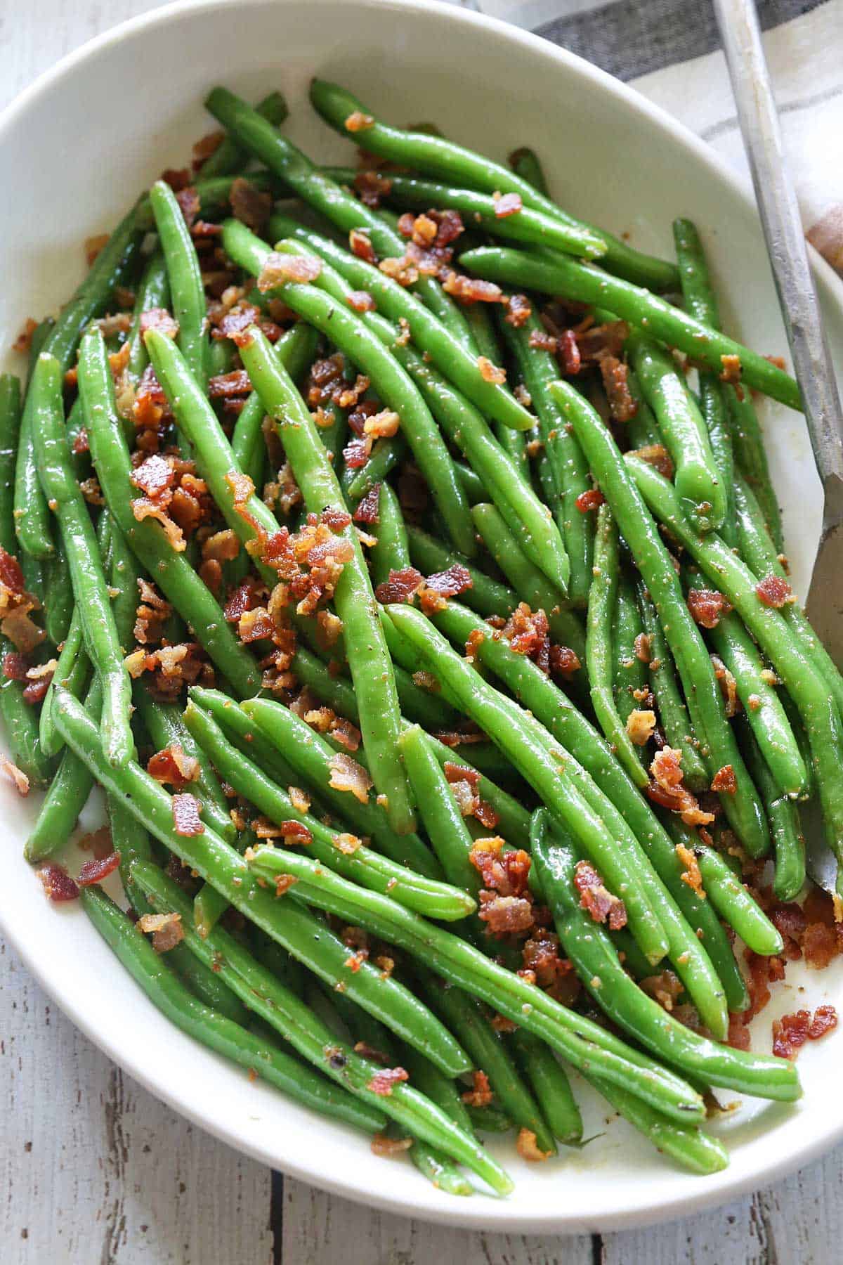 Green beans with bacon served with a serving spoon. 