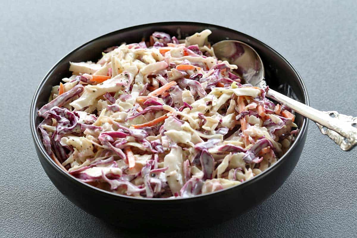 Homemade coleslaw served in a black bowl with a silver spoon. 