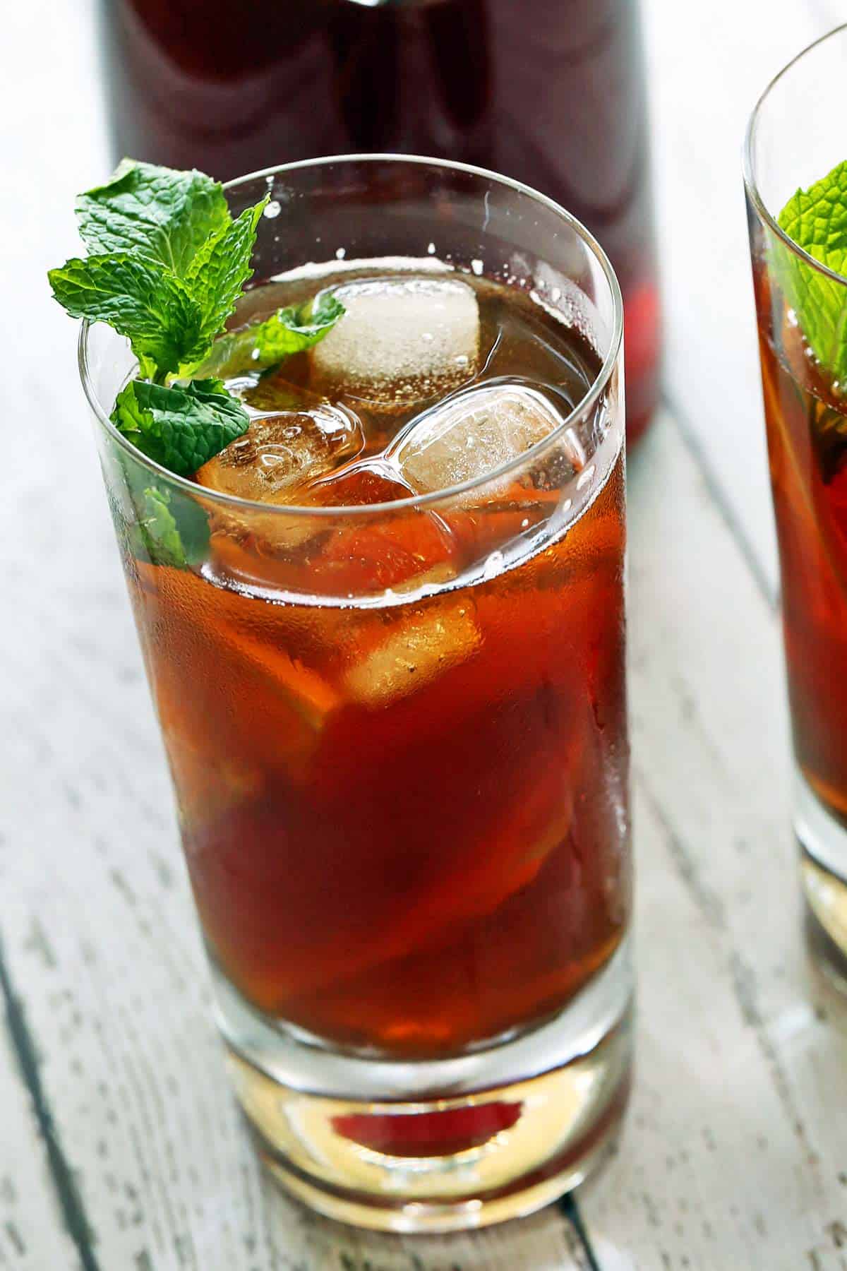 A tall glass filled with iced tea and garnished with mint leaves. 