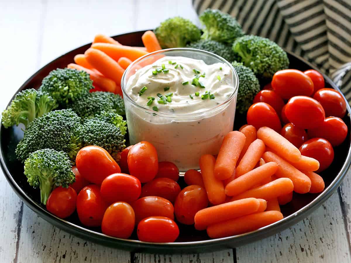 Sour cream dip served with fresh-cut vegetables on a dark platter. 