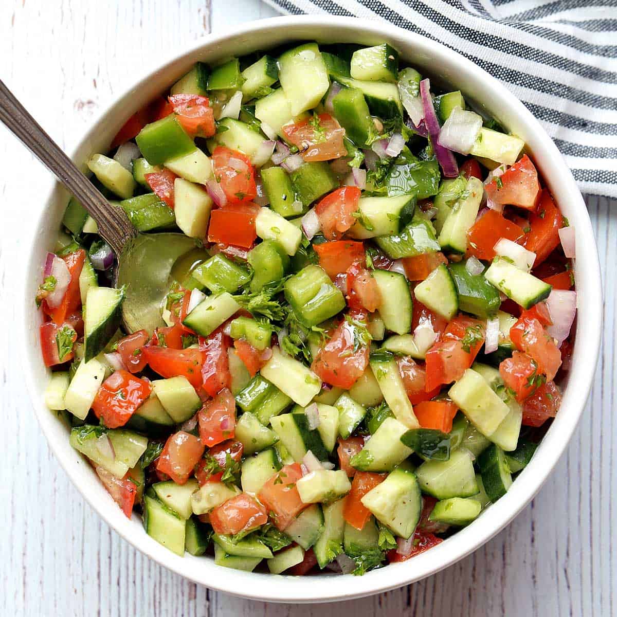 Israeli salad served in a white bowl with a serving spoon.