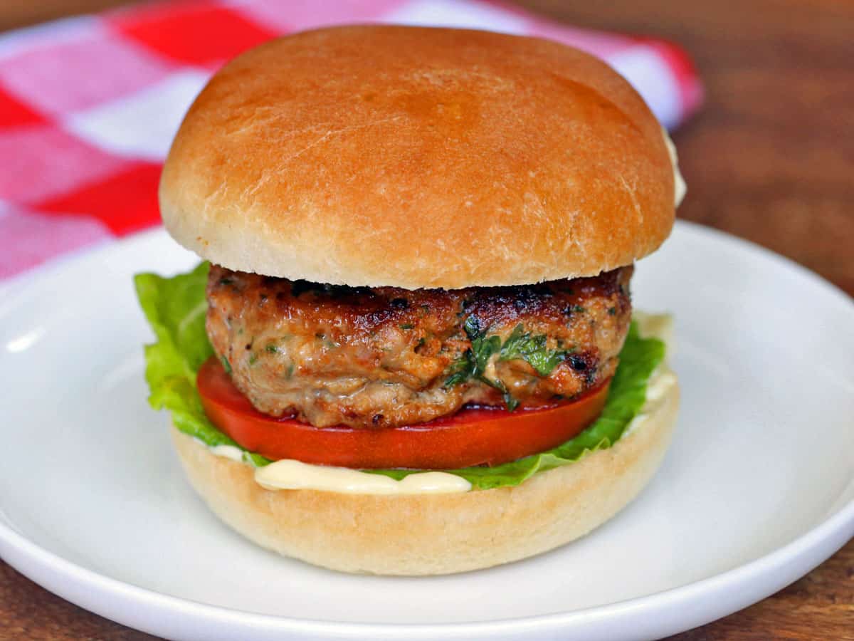 A turkey burger served on a plate, in a bun, with a napkin. 