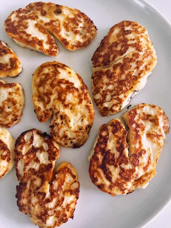 Pan-fried halloumi is served on a white plate.