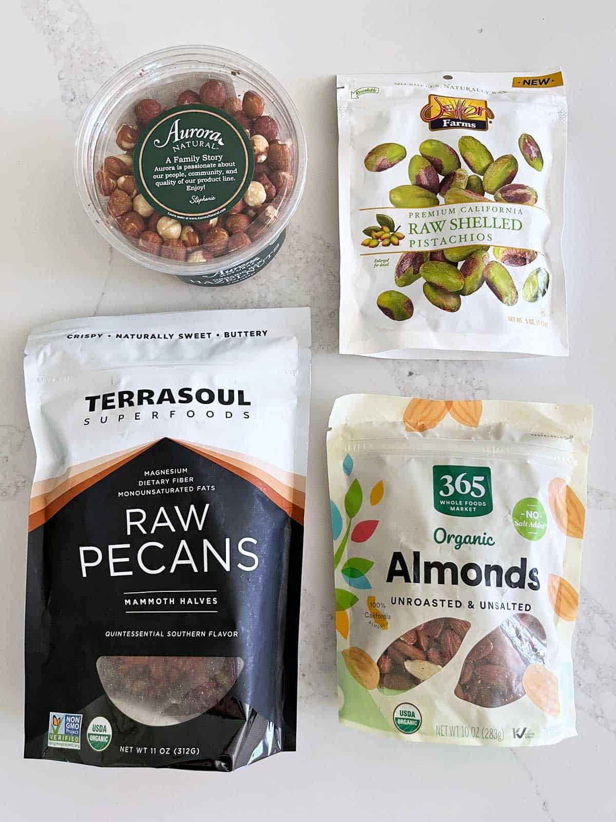 Four bags of packaged raw nuts: hazelnuts, pistachios, pecans, and almonds. 