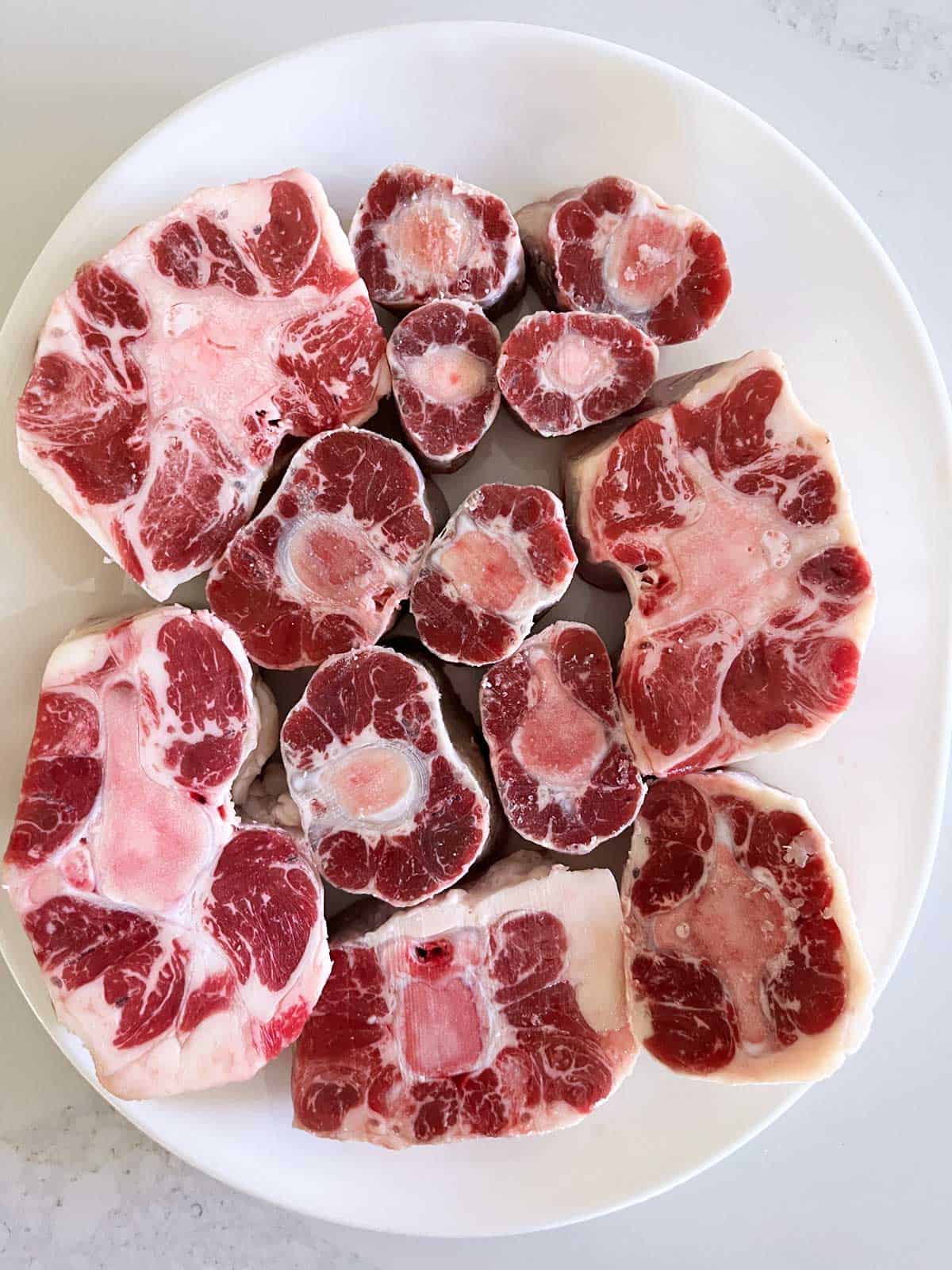 Different sizes of raw oxtails on a white platter. 