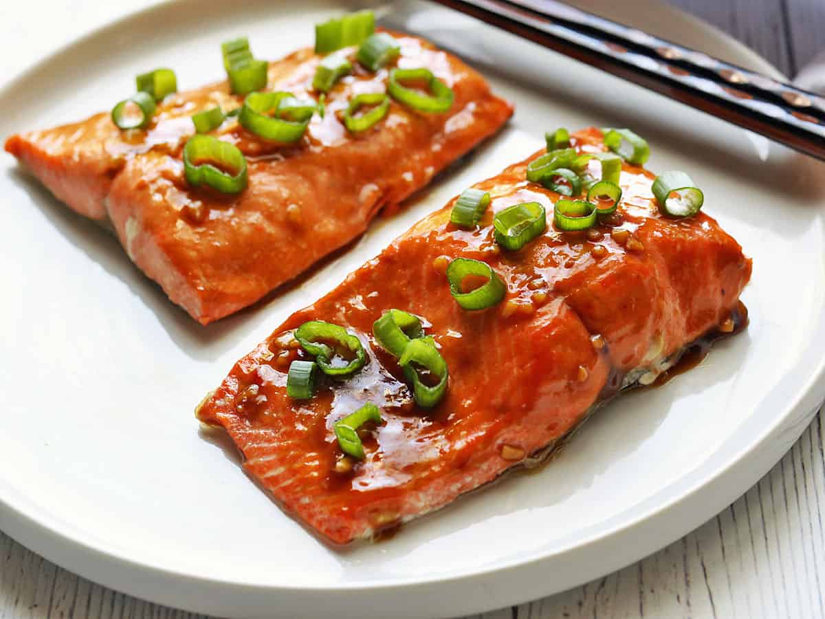 Asian salmon is served on a white plate with chopsticks. 